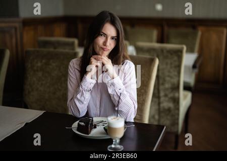 Junge, wunderschöne Brünette sitzt im Café, im Café, im Restaurant und krault ihr Gesicht hoch. Stockfoto