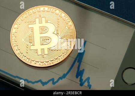 Konzeptionelle Kryptowährungs-Bitmünze auf einem Mobiltelefon mit einer Grafik im Hintergrund Stockfoto