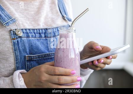 Weibliche Hände mit Blueberry Smoothie garniert mit Blaubeeren. Eine Frau, die ein Glas Frühstücksprotein-Smoothie trinkt. Verwenden Von Stockfoto