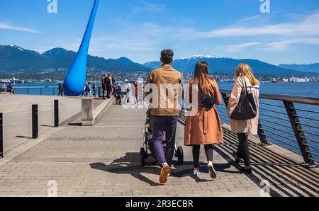 Junge Familie schiebt Kinderwagen und läuft auf dem Gehweg im Vancouver Urban Park Canada. Junge Familie, die mit einem Kinderwagen durch den Park spaziert Stockfoto