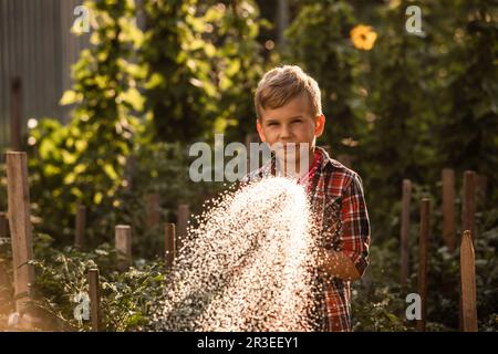 Der kleine Junge wäscht die Pflanzen und macht große Wasserspritzer Stockfoto