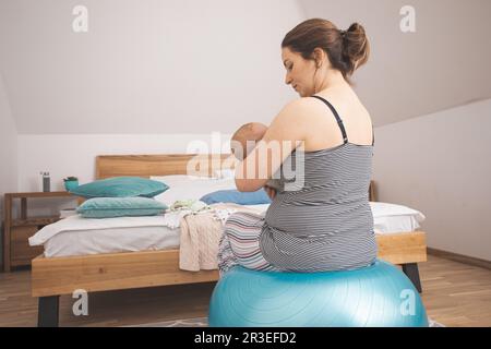 Mutter hält und schaukelt Baby auf fitball sitzen Stockfoto