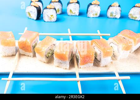Sushi-Brötchen mit Käse und Lachs, Käse, Daikon und scharfer Sauce auf blauem Hintergrund Stockfoto