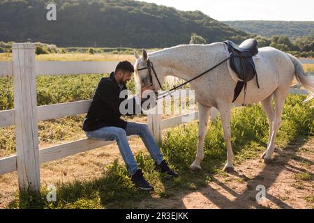 Der Mann ruht mit einem Pferd auf einer Ranch Stockfoto