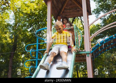 Die glücklichen kleinen Kinder im Begriff, auf dem Spielplatz zu rutschen Stockfoto