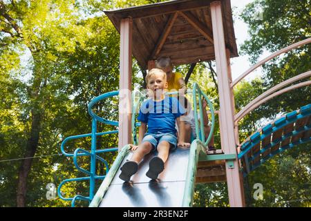 Die glücklichen kleinen Kinder im Begriff, auf dem Spielplatz zu rutschen Stockfoto