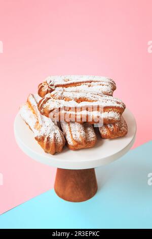 Hausgemachte Eclairs mit Puderzucker. Creme Puffs füllten Vanille-Vanille und waren mit Glasur auf hellem Hintergrund bedeckt. Profitero Stockfoto