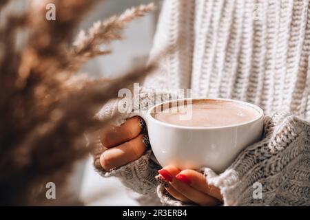 Pampas Gras und weibliche Hand halten weiße Tasse mit Kaffee. Trinken Cappuccino am Morgen Frühstück zu Hause. Ästhetik Stockfoto