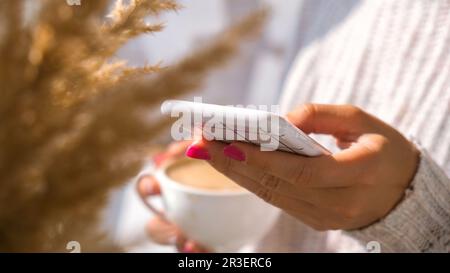 Frau mit Handy. Pampas Gras Wohndeko. Ich schaue in den sozialen Medien nach, während ich beim Frühstück Cappuccino trinke Stockfoto