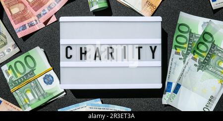 Leuchtkasten mit Wort CHARITY in schwarzen Buchstaben um Euro-Banknoten. Geld, Unternehmen, Finanzen, Investitionen, Sparen Stockfoto