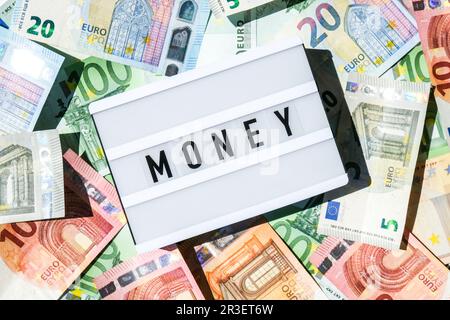 Lichtkastenbrett mit dem Wort GELD in schwarzen Buchstaben um die Euro-Banknoten. Finanzwesen. Geschäftlicher, finanzieller Erfolg und m Stockfoto