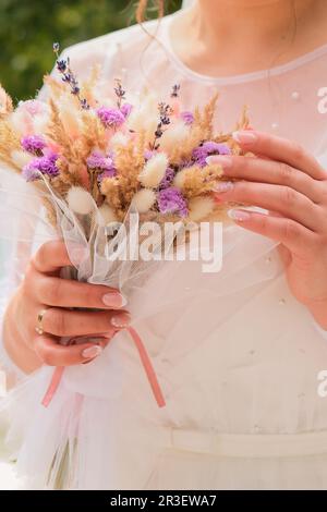 Unkrautblütenhintergrund in den Händen. Die Braut hält ihren Unkrautstrauß aus trockenen Blumen. Handgemachter Blumenstrauß Stockfoto