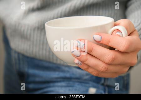 Handgemachte weibliche Hände mit weißer Kaffeetasse, stylischen blauen Nägeln und minimalistischem Design. Trendige Maniküre in modernem Design. Stockfoto