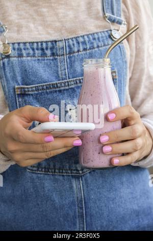 Weibliche Hände mit Blueberry Smoothie garniert mit Blaubeeren. Eine Frau, die ein Glas Frühstücksprotein-Smoothie trinkt. Verwenden Von Stockfoto