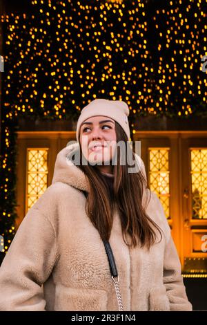 Junge, wunderschöne Frau, die auf einem im neuen Jahr dekorierten Straßenmarkt draußen spaziert. Atmosphäre eines traditionellen Weihnachtsmarktes. Porträt Stockfoto