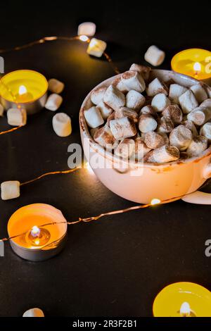 Tasse mit heißem Winter Kakao und Marshmallows in der Nacht. Weihnachtsbeleuchtung. Teelicht Kerzen. Gute Nacht süße Träume. Stockfoto