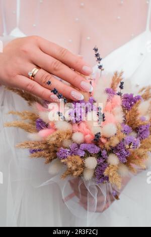 Unkrautblütenhintergrund in den Händen. Die Braut hält ihren Unkrautstrauß aus trockenen Blumen. Handgemachter Blumenstrauß Stockfoto
