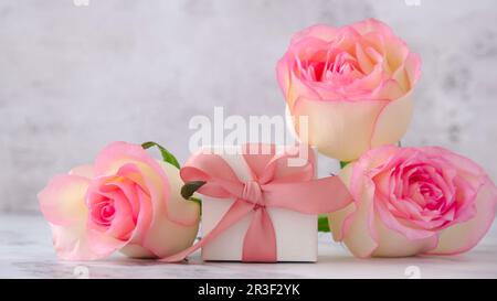 Geschenkbox mit Schleife, pinkfarbene Rosen auf pinkfarbenem Hintergrund. Grußkarte. Präsent für Frühlingsferien Kopierbereich für Text. Stockfoto