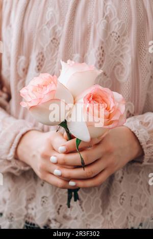 Weibliche Hand in rosafarbener Bluse mit zarter rosafarbener Rose. Minimale trendige Komposition. Abstrakte Kunstidee. Romantische pastellrosa Rosenfarbe Stockfoto