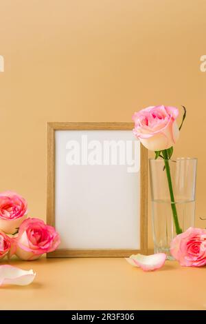 Holzrahmen mit leerem, weißem Papier und zarten Rosen auf beigefarbenem Hintergrund. Minimale trendige Komposition. Romantik Stockfoto