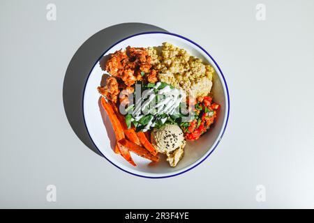 Vegetarische Schüssel mit Quinoa, Karotten, Blumenkohl in Sauce, Spinat, Tomaten und Hummus. Hartes Licht, tiefer Schatten Stockfoto