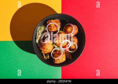 Salat mit frittierten Käsekugeln und roten Zwiebeln. Hartes Licht, tiefer Schatten Stockfoto