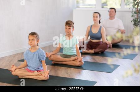 Teenager-Mädchen mit ihren Eltern praktiziert Yoga in Lotusposition Stockfoto