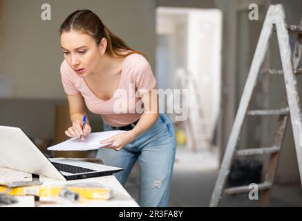 Frau mit Laptop im Haus wird gerade renoviert Stockfoto