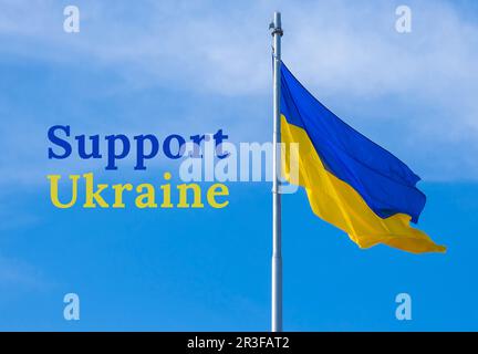 UNTERSTÜTZE DEN TEXT DER UKRAINE über die ukrainische Nationalflagge flattert im Wind gegen den blauen Himmel. Nationales Symbol des ukrainischen Volkes - Stockfoto