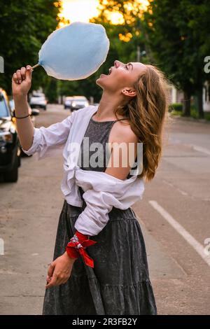 Süßes und hübsches junges Mädchen oder Student, isst und posiert mit zuckerblauer Zuckerwatte auf der Straße, Concept Happy Times. Lifestyl Stockfoto