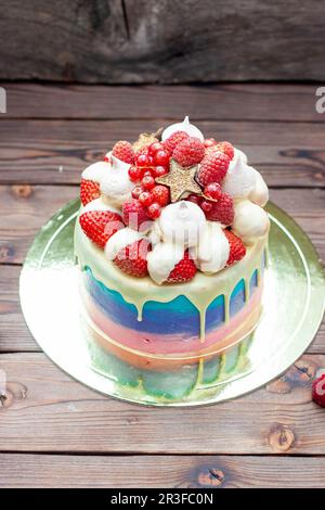 Rosafarbener, violetter und blauer Kuchen mit geschmolzener weißer Schokolade, frischen Erdbeeren in Schokolade getaucht, Himbeeren, roter Johannisbeere und Baiser Stockfoto