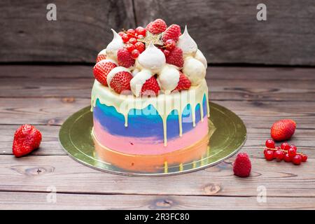 Rosafarbener, violetter und blauer Kuchen mit geschmolzener weißer Schokolade, frischen Erdbeeren in Schokolade getaucht, Himbeeren, roter Johannisbeere und Baiser Stockfoto