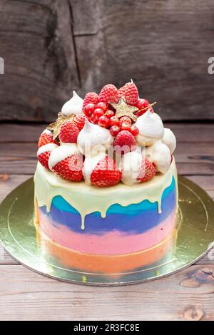 Rosafarbener, violetter und blauer Kuchen mit geschmolzener weißer Schokolade, frischen Erdbeeren in Schokolade getaucht, Himbeeren, roter Johannisbeere und Baiser Stockfoto