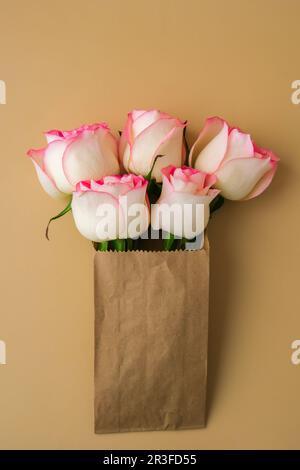 Zarte rosa Rosen in handgefertigter Papiertüte auf beigefarbenem Hintergrund. Minimale trendige Komposition. Abstrakte Kunstidee. Romantisches Pastellrosa Stockfoto