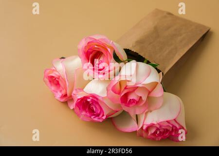 Zarte rosa Rosen in handgefertigter Papiertüte auf beigefarbenem Hintergrund. Minimale trendige Komposition. Abstrakte Kunstidee. Romantisches Pastellrosa Stockfoto