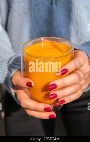 Eine unbekannte Frau, die Kürbis-Smoothie-Latte in der Hand hat. Herbstkaffee mit würzigem Kürbisgeschmack, heißes Getränk der Saison. Herbst-Dri Stockfoto