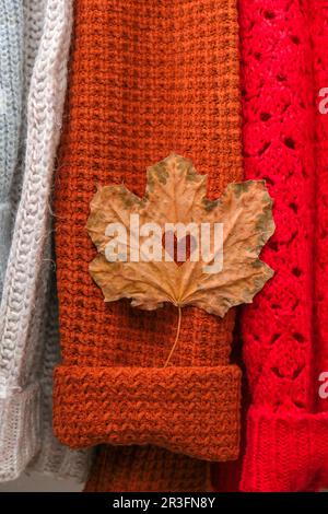 Herbstkonzept. Herzzaugliches Ahornblatt auf kuschelig warmem Pullover. Strickpullover aus Wolle und Mohair. Hygge-Stil Stockfoto