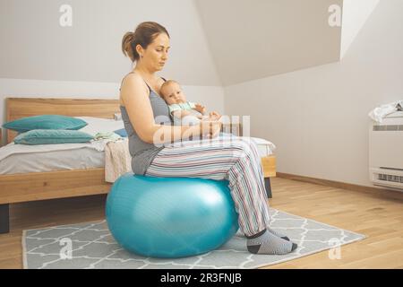 Mutter hält und schaukelt Baby auf fitball sitzen Stockfoto