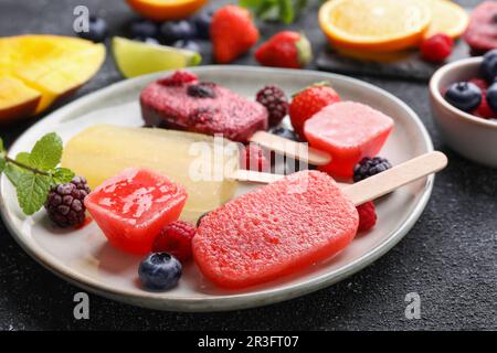 Teller mit verschiedenen leckeren Eiswürfeln auf einem schwarz strukturierten Tisch, Nahaufnahme. Obst-Eis-Eis-Eis Stockfoto