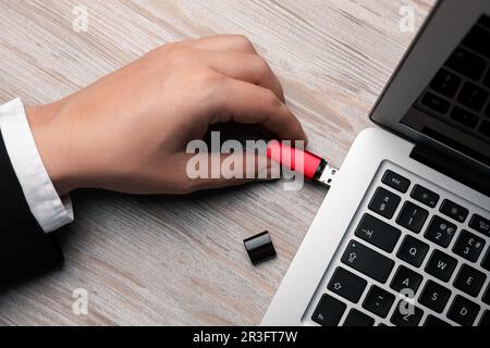 Mann, der ein usb-Flash-Laufwerk an einen Laptop am weißen Holztisch anschließt, Draufsicht Stockfoto