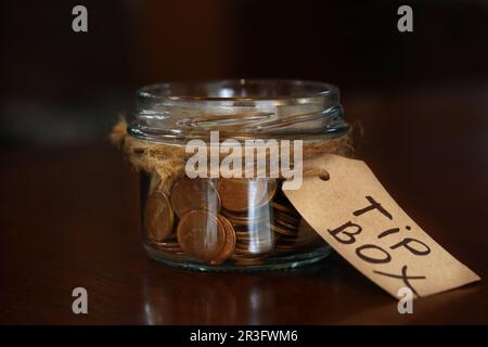 Ein Trinkgeldkasten voll mit Münzen auf einem Holztisch im Café, Schließung Stockfoto