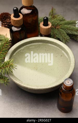 Schüssel mit ätherischem Öl und Tannenzweigen auf grauem Tisch. Aromatherapie Stockfoto