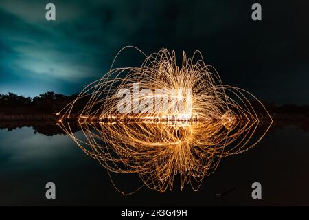 Wunderschöne Figuren und Lichtblitze, die sich nachts in einem See spiegeln. Stockfoto