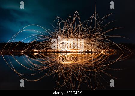 Wunderschöne Figuren und Lichtblitze, die sich nachts in einem See spiegeln. Stockfoto