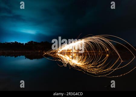 Wunderschöne Figuren und Lichtblitze, die sich nachts in einem See spiegeln. Stockfoto