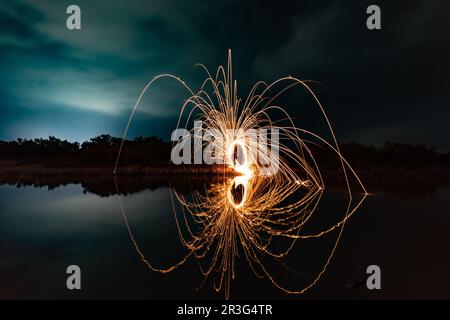 Wunderschöne Figuren und Lichtblitze, die sich nachts in einem See spiegeln. Stockfoto