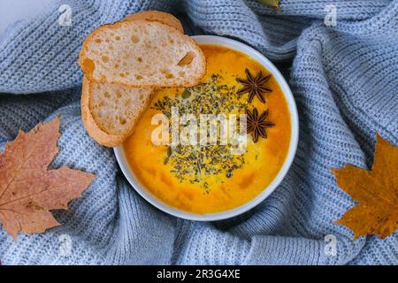 Hausgemachte Karotten, Ingwer, Curcuma, scharfe Suppe. Traditionelle Kürbissuppe der Saison mit cremiger seidiger Textur im gemütlichen Pullover Stockfoto