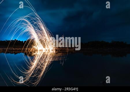 Wunderschöne Figuren und Lichtblitze, die sich nachts in einem See spiegeln. Stockfoto