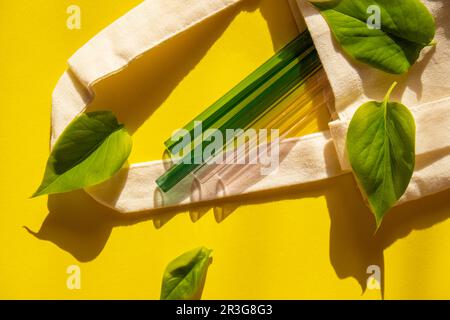 Wiederverwendbare Strohhalme aus Glas auf farbenfrohem Hintergrund mit grünen Blättern in einem umweltfreundlichen Trinkhalm-Set Wiederverwendbarer bequemer RO Stockfoto