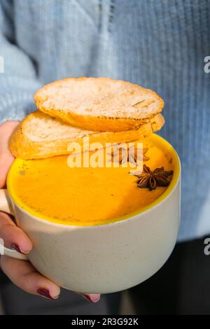 Eine Frau mit hausgemachter Karotte, Ingwerkurcuma, scharfer Suppe. Traditionelle Kürbissuppe der Saison mit cremiger, seidiger Konsistenz. Gesunde ve Stockfoto